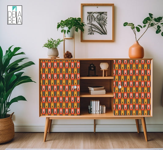 A vinyl wrap with a geometric pattern featuring hexagons in various colors applied to a wooden furniture piece, possibly a sideboard or cabinet, in a room with a plant, decorative items, and a framed picture on the wall.