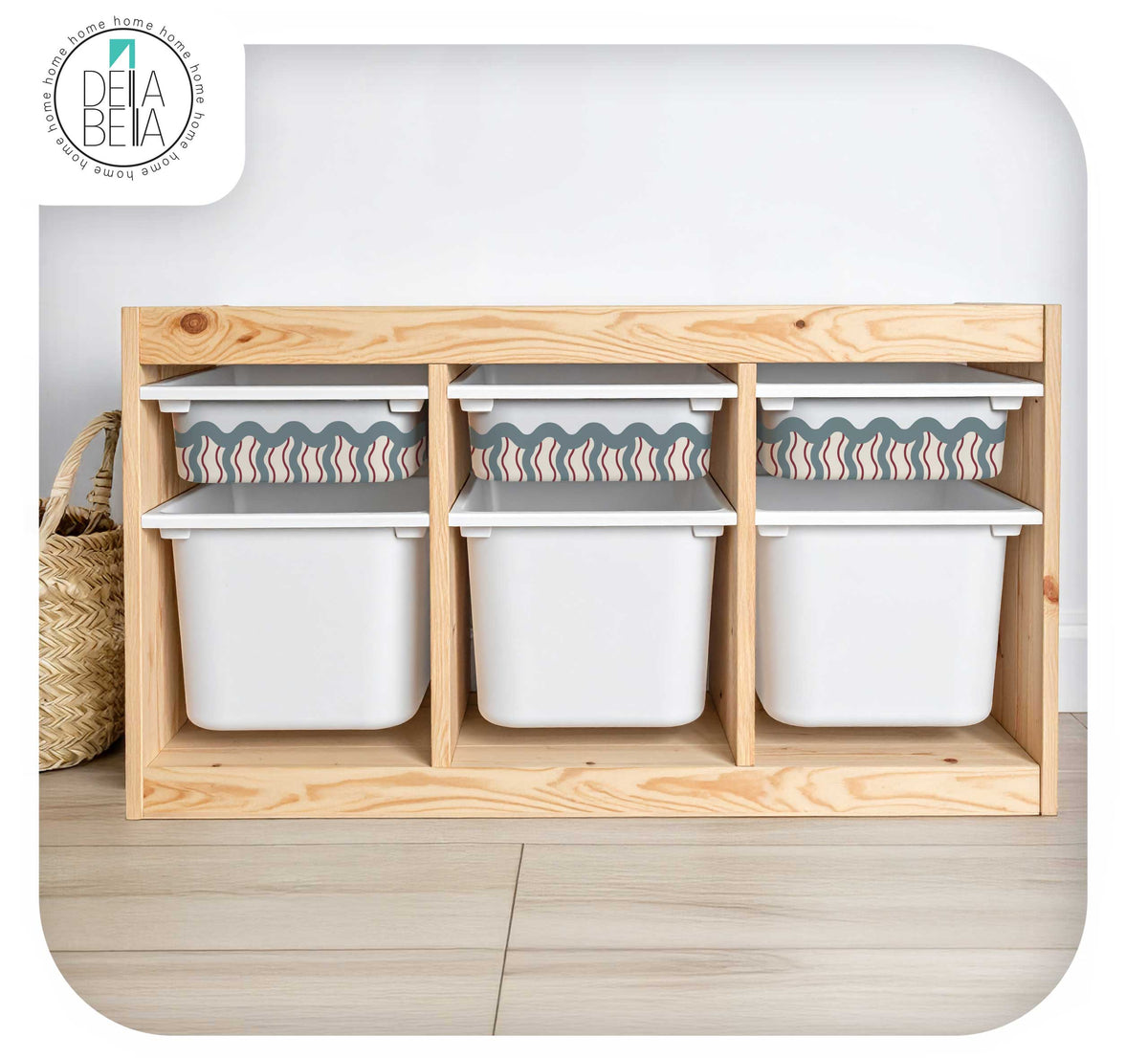 A light natural trofast  storage organizer with three open compartments holding white plastic bins, shown against a white wall and light wood floor. A woven basket is partially visible on the left, and a Dela Benta logo appears in the top-left corner.